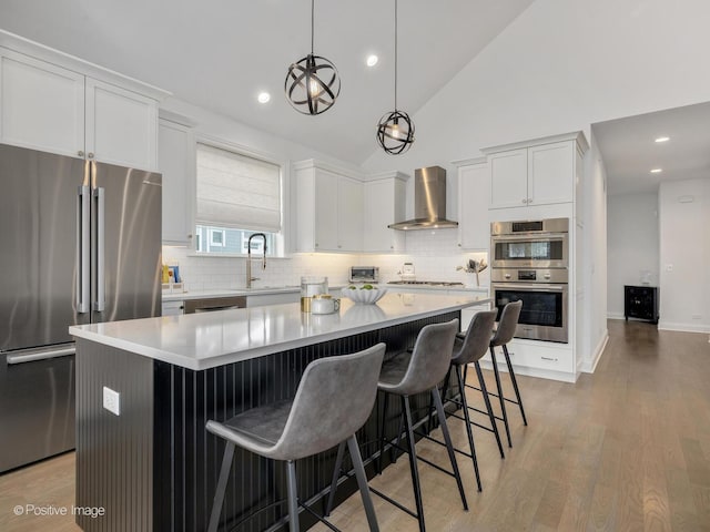 kitchen with white cabinetry, a kitchen island, pendant lighting, stainless steel appliances, and wall chimney range hood