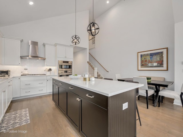 kitchen featuring white cabinetry, wall chimney range hood, decorative light fixtures, and a kitchen island