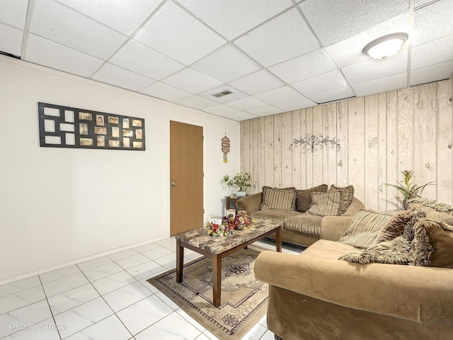 living room with tile patterned floors, wood walls, and a drop ceiling