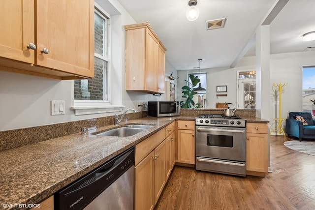 kitchen featuring hardwood / wood-style floors, stainless steel appliances, dark stone counters, sink, and kitchen peninsula