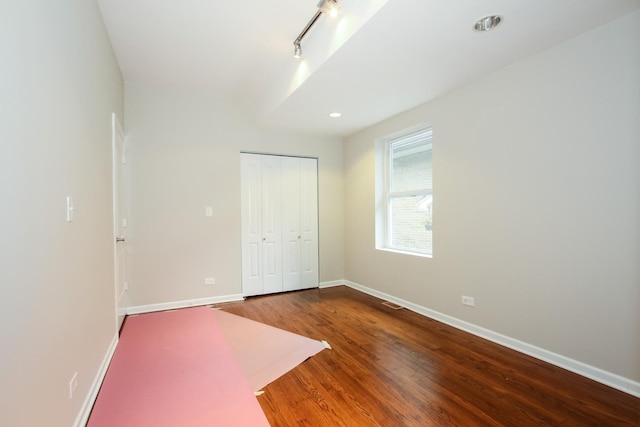 unfurnished bedroom with rail lighting, hardwood / wood-style flooring, and a closet