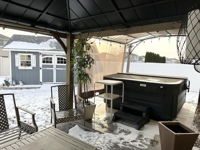 snow covered patio with a gazebo, a hot tub, and a storage shed