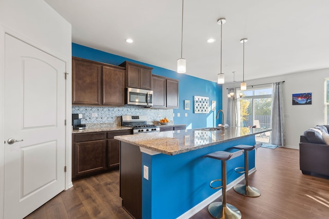 kitchen with sink, stainless steel appliances, light stone counters, an island with sink, and decorative light fixtures