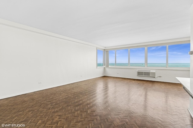 spare room featuring a wall mounted air conditioner, dark parquet flooring, a wealth of natural light, and a water view