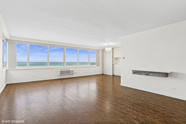 unfurnished living room with a water view, a wall unit AC, an inviting chandelier, and dark parquet floors