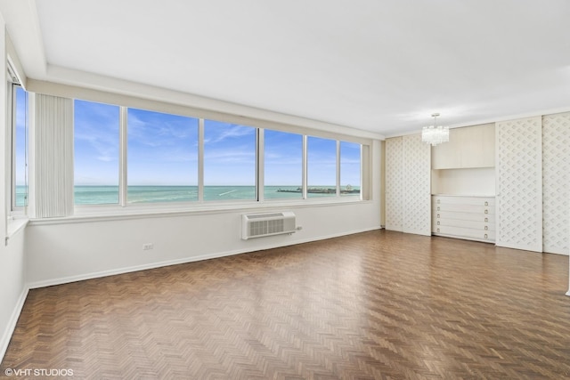 spare room with a view of the beach, a wall mounted AC, a water view, a notable chandelier, and dark parquet floors