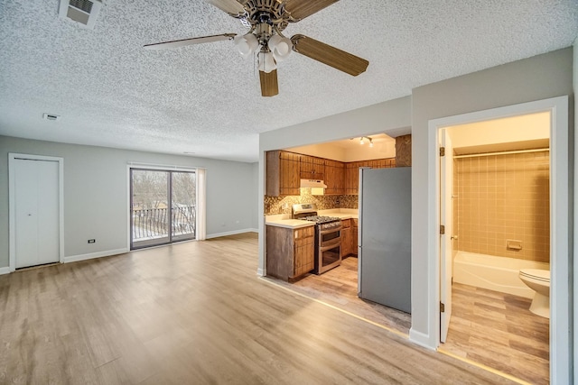 kitchen with ceiling fan, decorative backsplash, light wood-type flooring, a textured ceiling, and appliances with stainless steel finishes