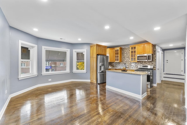 kitchen featuring appliances with stainless steel finishes, backsplash, dark hardwood / wood-style flooring, light stone counters, and a center island