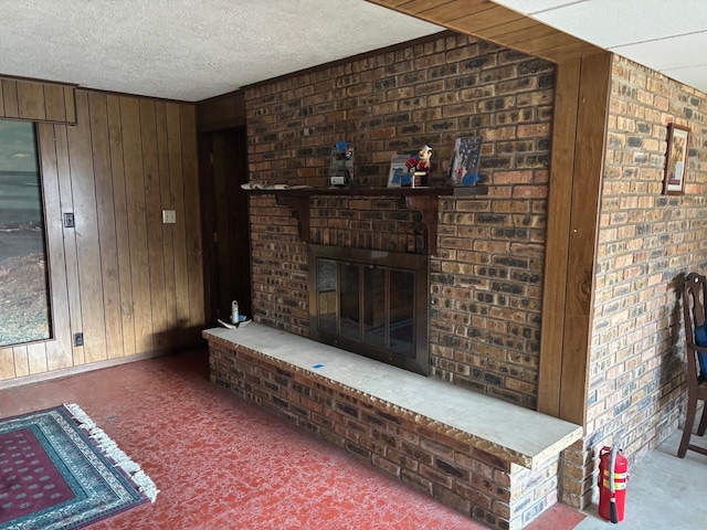 living room featuring a brick fireplace, a textured ceiling, and wooden walls