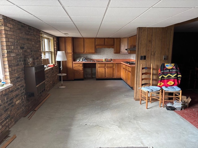 kitchen featuring heating unit, sink, brick wall, and concrete flooring