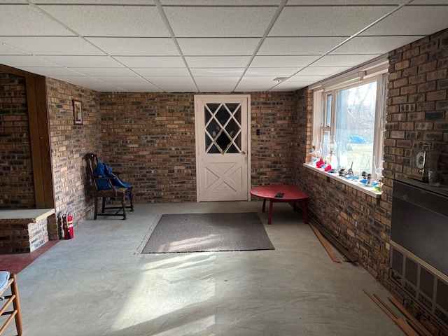 interior space featuring brick wall, a paneled ceiling, and concrete flooring