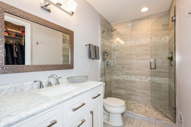 bathroom featuring a walk in closet, a shower stall, toilet, and vanity