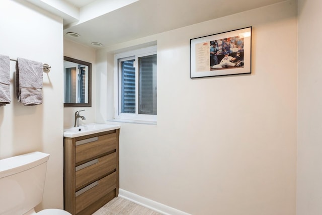 half bathroom featuring toilet, baseboards, and vanity