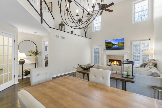 dining space featuring dark hardwood / wood-style floors, ceiling fan, a towering ceiling, and a tile fireplace