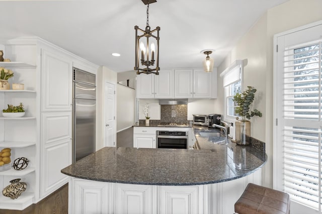 kitchen with kitchen peninsula, appliances with stainless steel finishes, sink, decorative light fixtures, and white cabinetry