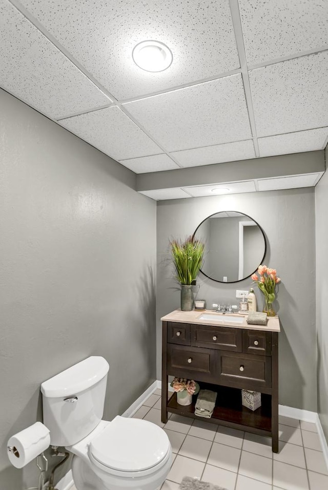 bathroom with a paneled ceiling, tile patterned flooring, vanity, and toilet