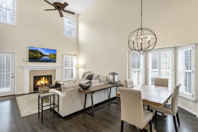 dining space featuring ceiling fan with notable chandelier, a healthy amount of sunlight, dark hardwood / wood-style flooring, and a fireplace