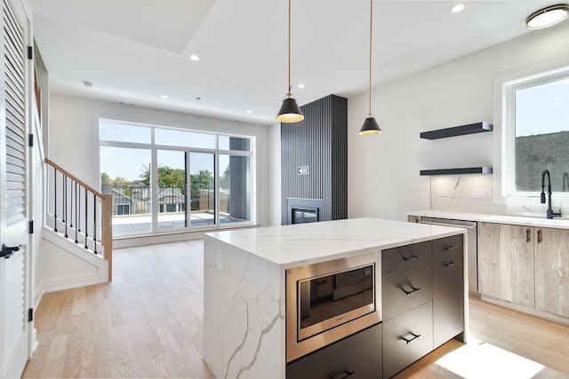 kitchen featuring decorative light fixtures, light hardwood / wood-style flooring, light stone countertops, a kitchen island, and stainless steel microwave