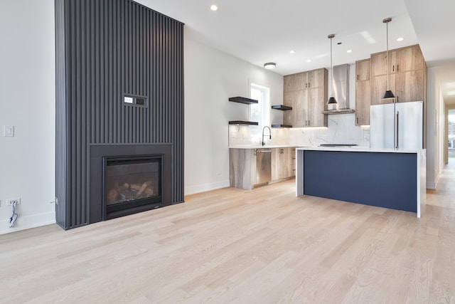 kitchen with stainless steel appliances, a center island, light hardwood / wood-style flooring, hanging light fixtures, and wall chimney range hood