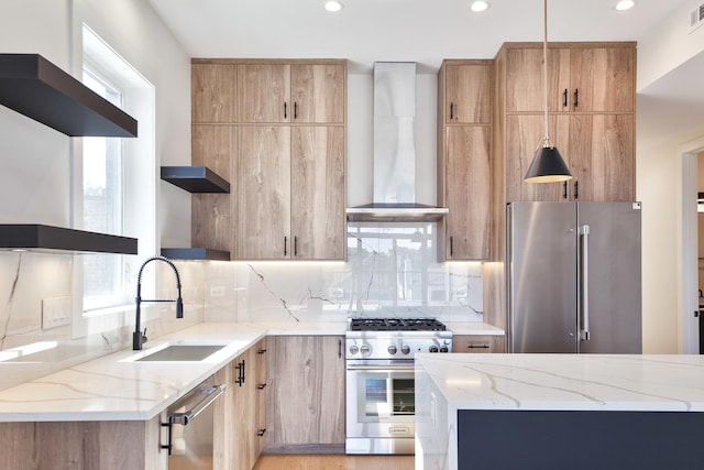 kitchen featuring sink, wall chimney range hood, high quality appliances, and light stone counters