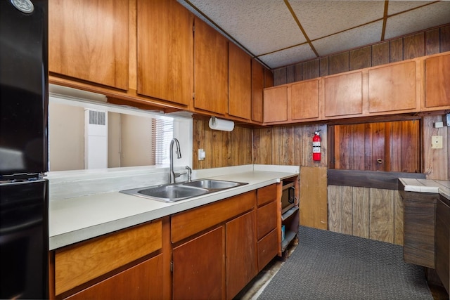 kitchen with a paneled ceiling, wood walls, sink, and refrigerator