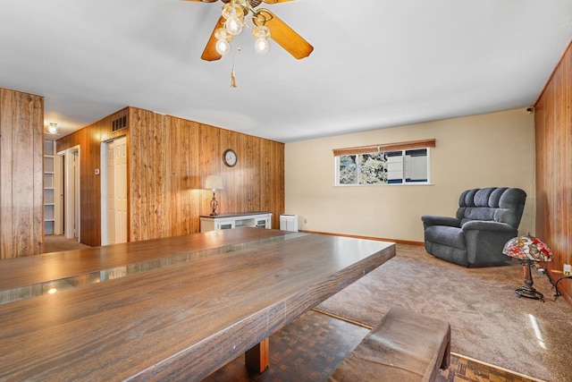 dining room featuring ceiling fan, wooden walls, and carpet