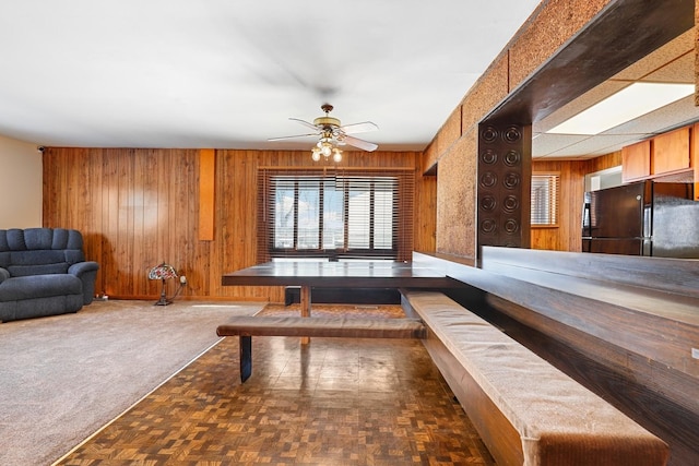 interior space with ceiling fan, wooden walls, and dark parquet floors