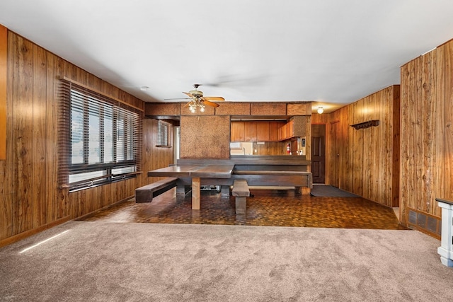 carpeted dining room with wood walls and ceiling fan