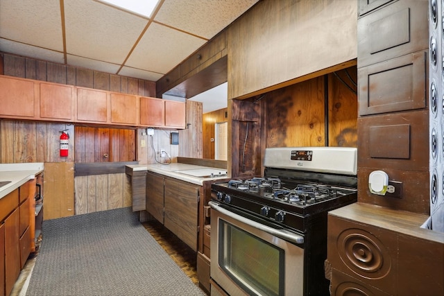 kitchen with stainless steel gas stove, wood walls, and a drop ceiling