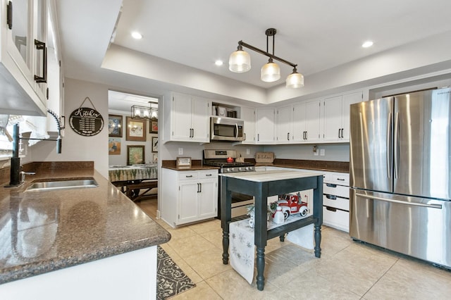 kitchen with dark stone counters, stainless steel appliances, sink, white cabinets, and hanging light fixtures