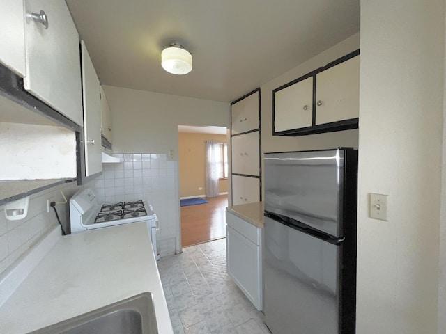 kitchen with sink, stainless steel refrigerator, white cabinets, white range with gas cooktop, and decorative backsplash