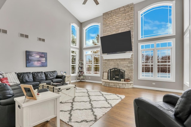 living room featuring hardwood / wood-style floors, a stone fireplace, ceiling fan, a towering ceiling, and a wealth of natural light