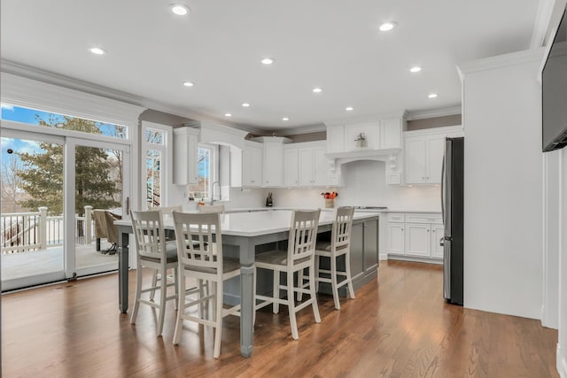 kitchen with stainless steel refrigerator, wood-type flooring, decorative backsplash, a breakfast bar, and white cabinets