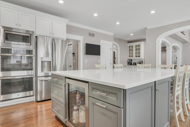 kitchen with a kitchen bar, gray cabinets, beverage cooler, and appliances with stainless steel finishes