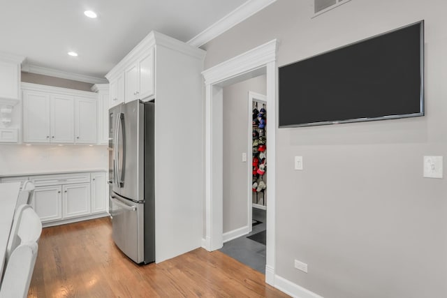 kitchen with white cabinets, stainless steel fridge, light hardwood / wood-style floors, and ornamental molding