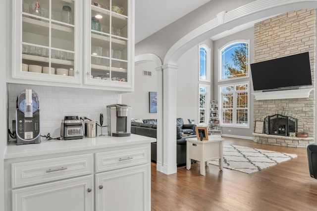 bar featuring decorative backsplash, dark wood-type flooring, white cabinets, a high ceiling, and a stone fireplace