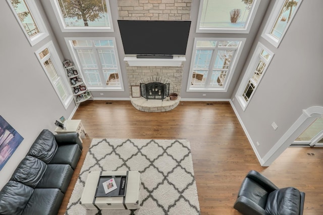 living room with a towering ceiling, hardwood / wood-style flooring, and a stone fireplace