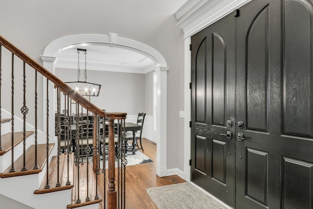 entryway featuring wood-type flooring, ornate columns, ornamental molding, and a notable chandelier