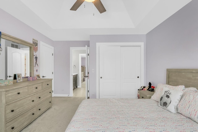 bedroom with a raised ceiling, ceiling fan, a closet, and light colored carpet