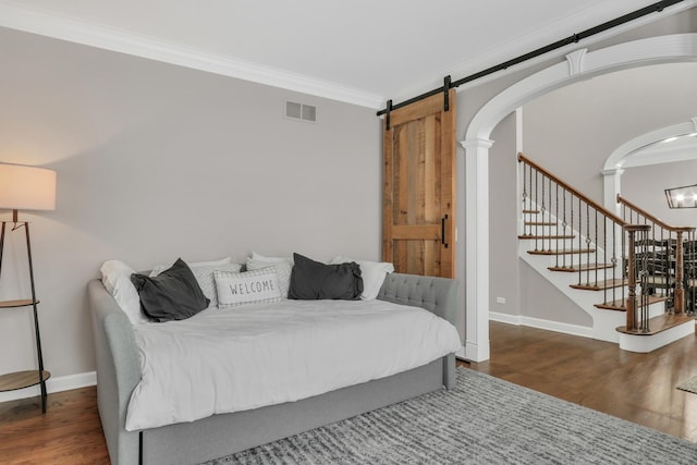 bedroom featuring a barn door, dark hardwood / wood-style flooring, and ornamental molding