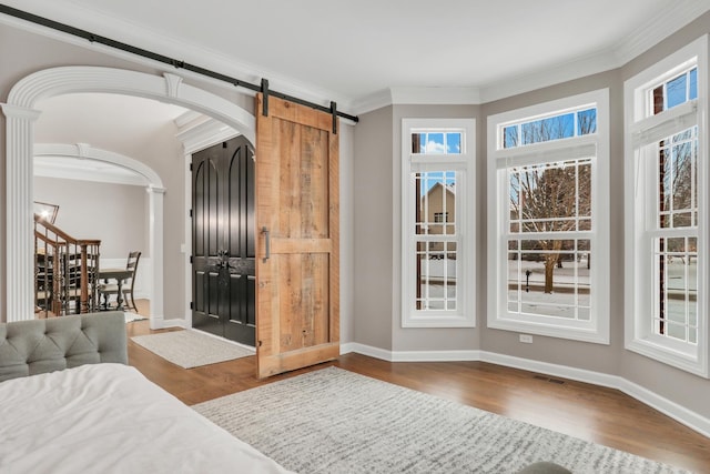 bedroom featuring a barn door, crown molding, and dark wood-type flooring