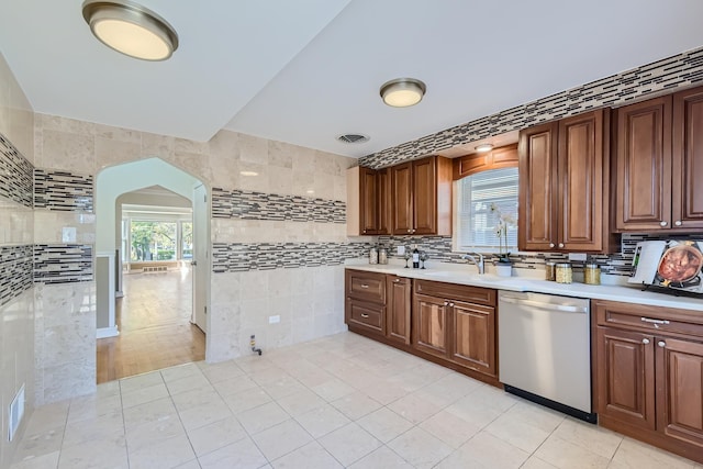 kitchen featuring backsplash, sink, stainless steel dishwasher, tile walls, and light tile patterned flooring