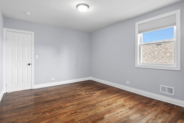 empty room with dark wood-style floors, visible vents, and baseboards