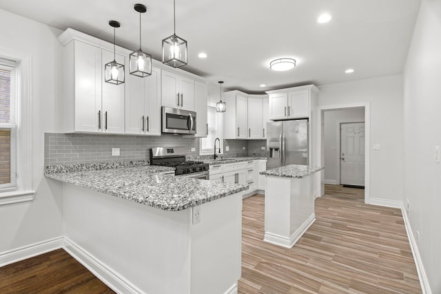 kitchen with light stone countertops, light wood finished floors, a peninsula, stainless steel appliances, and white cabinetry