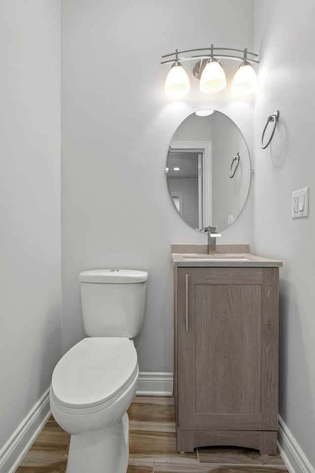 bathroom with toilet, vanity, baseboards, and wood finished floors