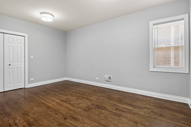 empty room featuring visible vents, dark wood-type flooring, and baseboards