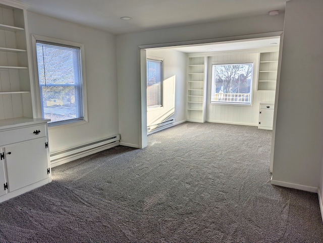 carpeted spare room with built in shelves, a wealth of natural light, and a baseboard heating unit