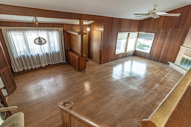 unfurnished living room featuring ceiling fan, a healthy amount of sunlight, wood walls, and a brick fireplace