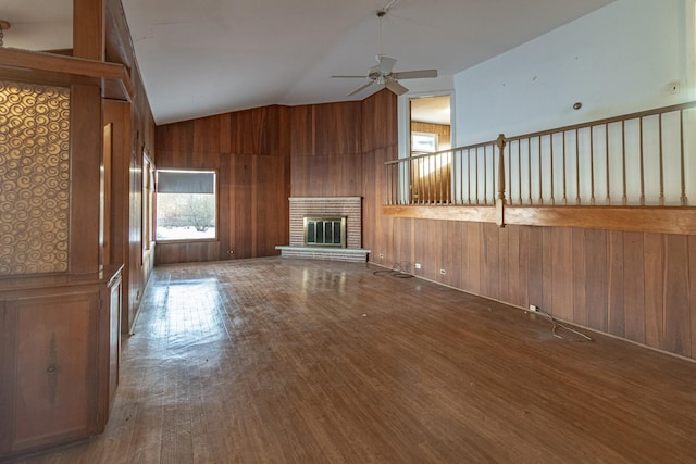 unfurnished living room with ceiling fan, a brick fireplace, wood walls, lofted ceiling, and hardwood / wood-style flooring