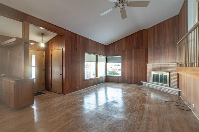 unfurnished living room featuring wooden walls, vaulted ceiling, ceiling fan, a fireplace, and wood-type flooring